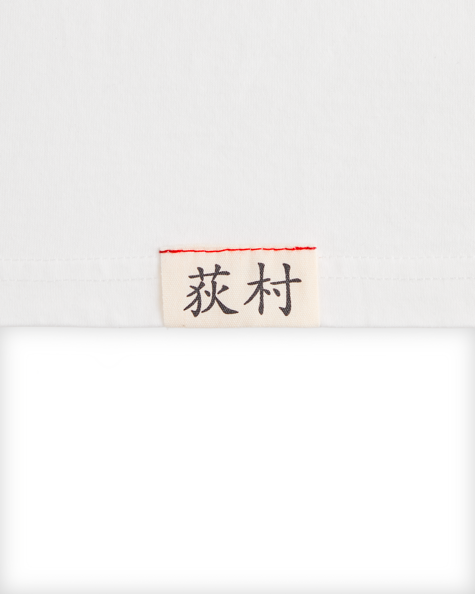 Close-up of the woven Ichiro Ogimura name label on the white Koyo Bear OGI Signature Serve T-shirt.