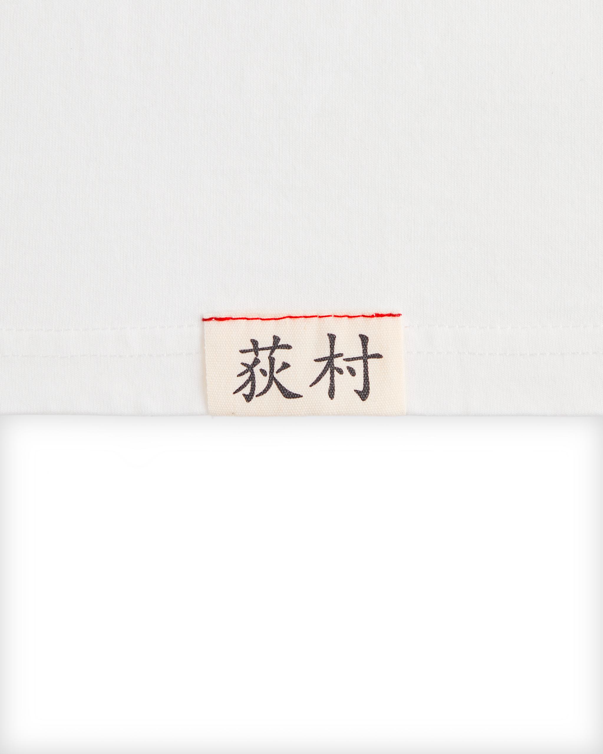 Close-up of the woven Ichiro Ogimura name label on the white Koyo Bear OGI Signature Serve T-shirt.