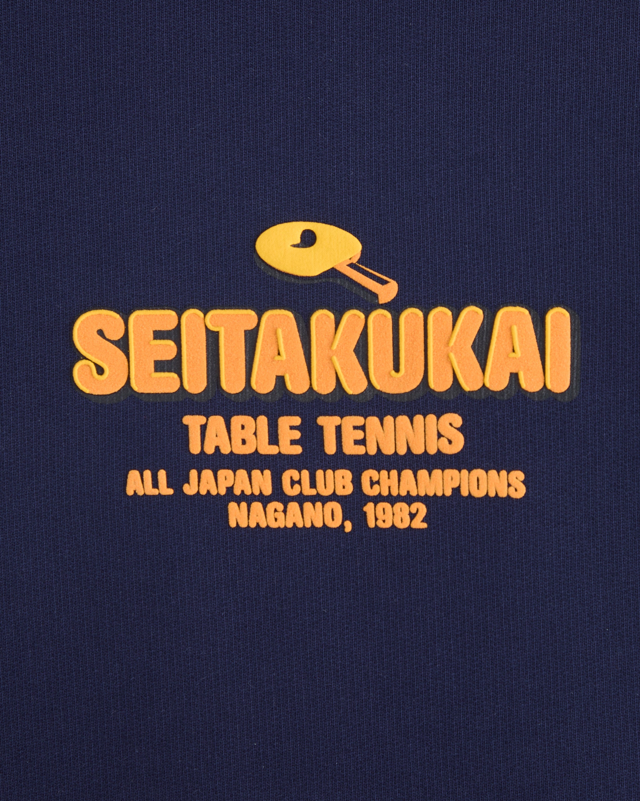 Front print detail of the navy Koyo Bear Team SEITAKUKAI hoodie featuring the yellow table tennis club logo from the 1982 Nagano champions.
