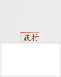 Close-up of the woven Ichiro Ogimura name label on the white Koyo Bear OGI Signature Serve T-shirt.