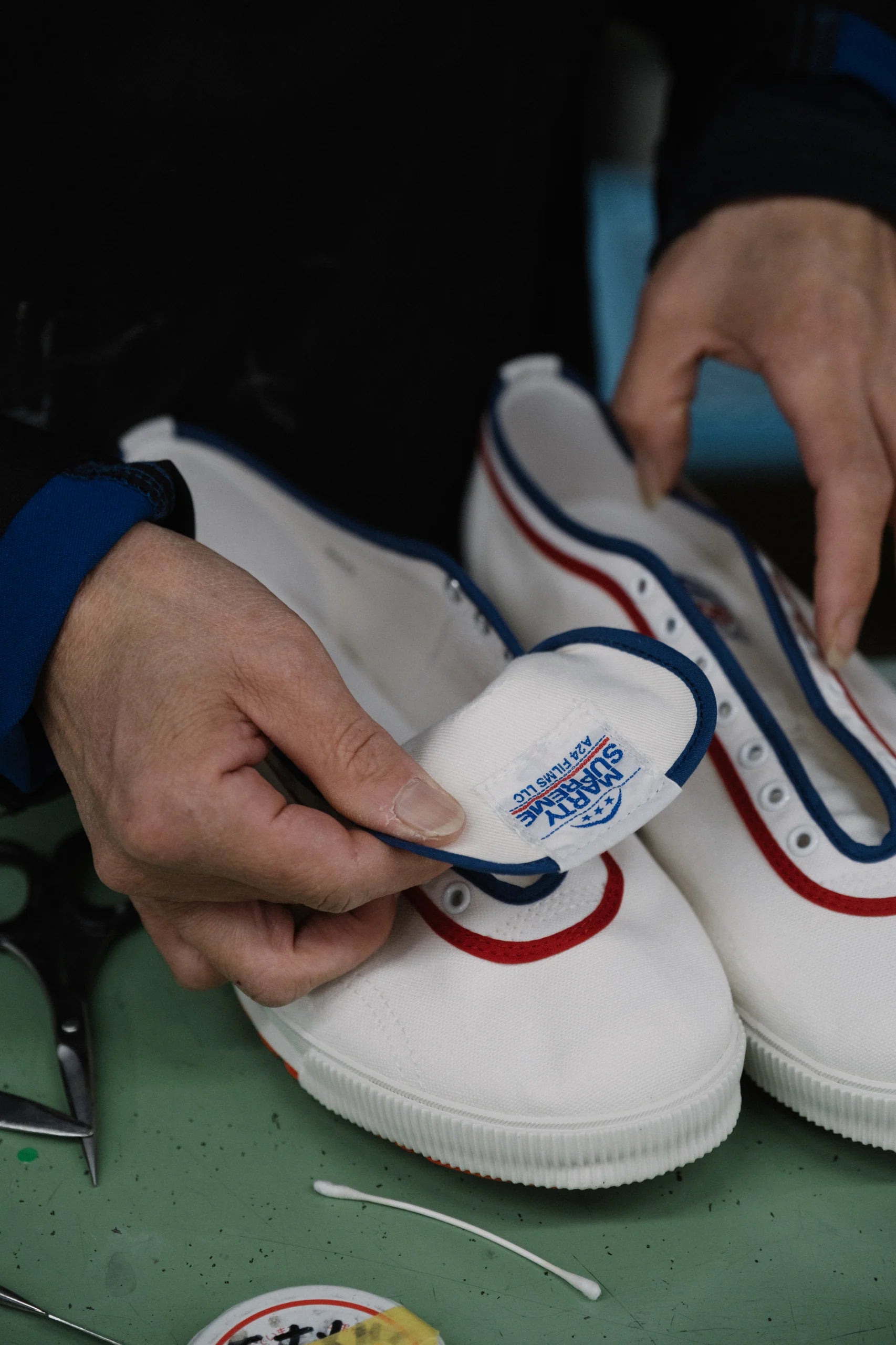 Close-up of hands inspecting the Made in Japan label inside Koyo Bear Marty Supreme table tennis shoes during production.